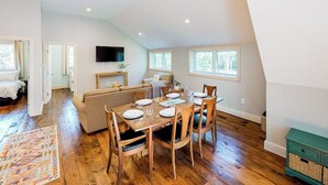 Un coin repas avec une table en bois dressée pour quatre personnes, un canapé et un téléviseur fixé au mur.