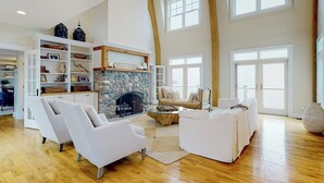 A spacious living room with a stone fireplace, white sofas, and a high ceiling with large windows. - Spectacular oceanfront retreat with amazing views, sunroom & washer/dryer (Georgetown)