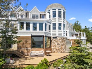 A large, modern house with multiple levels, a prominent corner turret, and a spacious outdoor deck area.