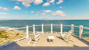 A wooden deck with white chairs and a table overlooking the ocean. - Spectacular oceanfront retreat with amazing views, sunroom & washer/dryer (Georgetown)