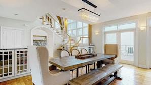 A dining area with a wooden table, benches, and a staircase with a chandelier. - Spectacular oceanfront retreat with amazing views, sunroom & washer/dryer (Georgetown)