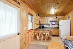 A wooden cabin interior with a kitchen, bar stools, and a sofa.