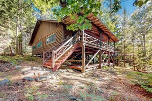 Una cabana de fusta amb una escala que mena a una terrassa, envoltada d'arbres.