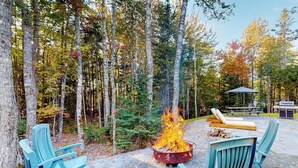 A forest setting with a fire pit, outdoor seating, and a picnic table. - Contemporary retreat with grill, firepit, & patio - walk to beach (Lamoine)