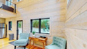 A modern interior with wooden walls, a dining area with a wooden table and chairs, and large windows offering a view of the outdoors. - Contemporary retreat with grill, firepit, & patio - walk to beach (Lamoine)