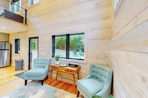 A modern interior with wooden walls, a dining area with a wooden table and chairs, and large windows offering a view of the outdoors.