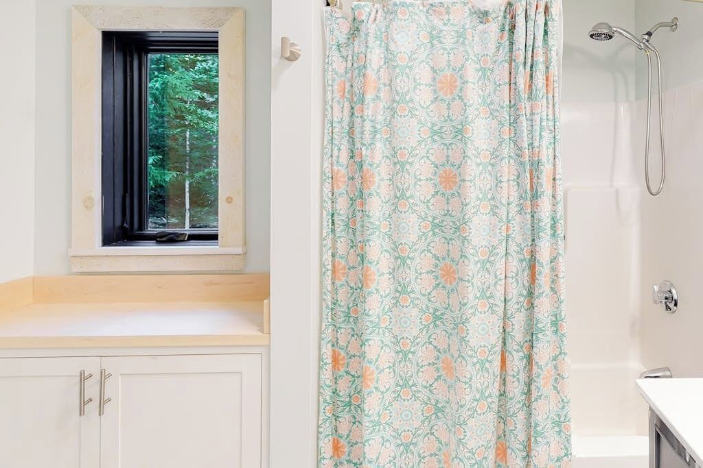 A bathroom with a window, a shower, and a patterned curtain.