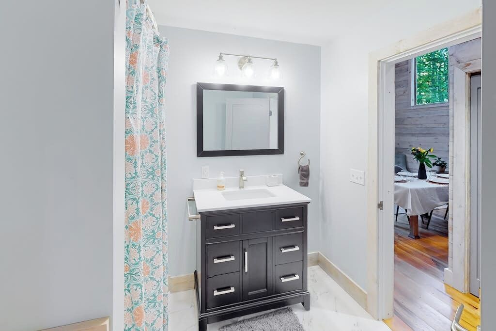 A bathroom with a dark vanity, a mirror, and a shower curtain.