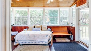 Quarto com cama, um banco, janela e porta.