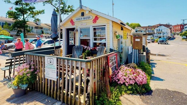 En liten träbyggnad med en skylt där det står   ”Hamnkapten”, omgiven av ett trästaket och krukväxter.