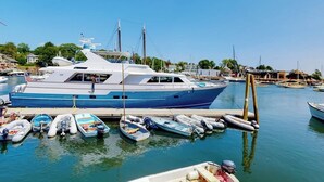 En småbåtshamn med en stor lyxyacht förtöjd vid en träbrygga, omgiven av mindre båtar.