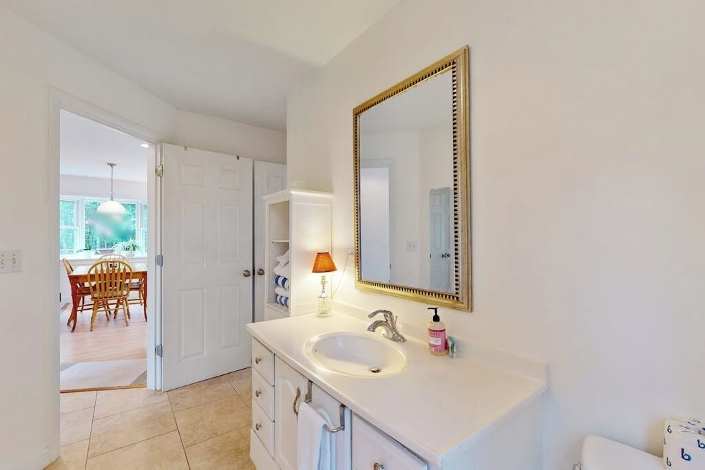 A bathroom with a white sink, a large mirror, and a door leading to a dining area.