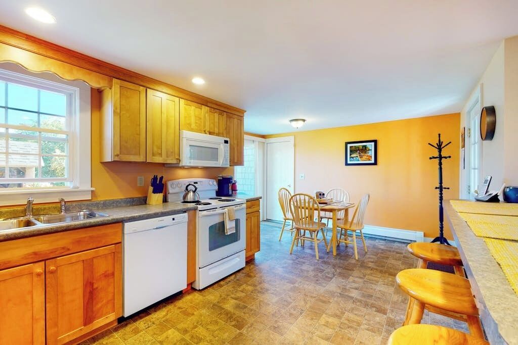 Una cocina con armarios de madera, microondas, estufa y un comedor con sillas y mesa.