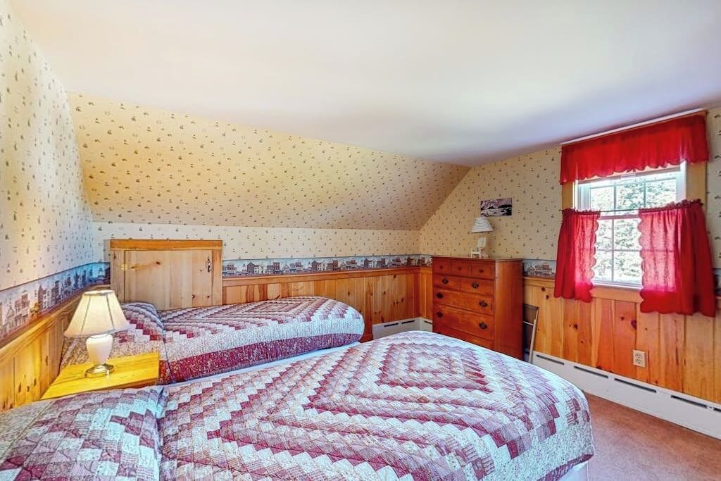 Een slaapkamer met twee bedden, een houten dressoir, een raam met rode gordijnen en een muur met een stadsgezicht muurschildering.