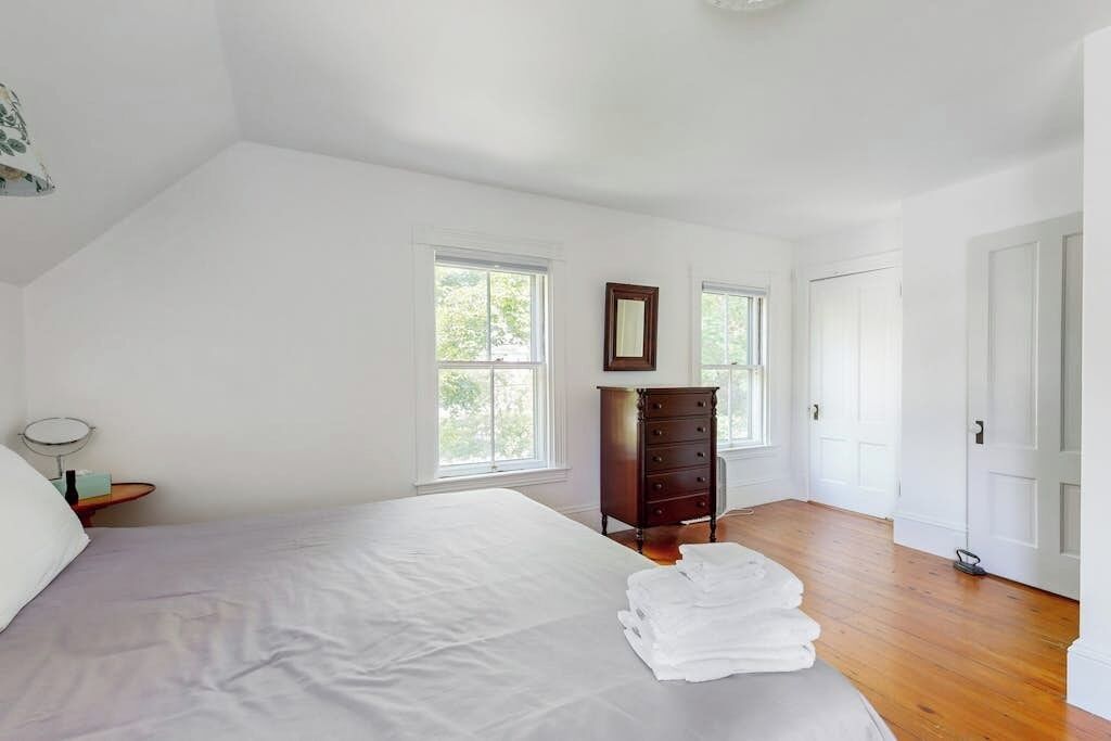 A bedroom with a bed, a dresser, two windows, and a door.