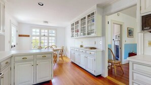 Una cocina con muebles blancos, una mesa de comedor con sillas y un ventanal.