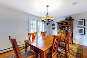 Een eetkamer met een houten tafel en stoelen, een kroonluchter en een kast met servies.