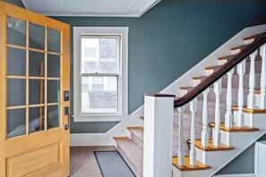Una escalera con balaustres blancos y barandillas de madera, una puerta con paneles de vidrio y una ventana con persianas.