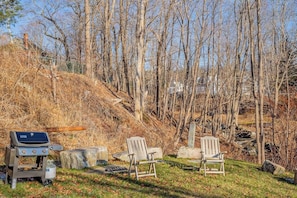 Un patio trasero con una parrilla, dos sillas Adirondack y un muro de piedra.