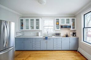 Une cuisine moderne avec des meubles gris, un réfrigérateur en acier inoxydable, une fenêtre et un four à micro-ondes.