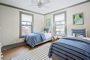 Une chambre avec deux lits, un ventilateur de plafond et de grandes fenêtres.