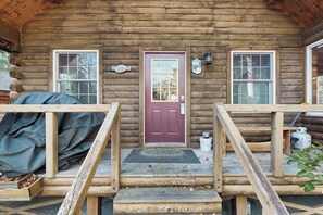 Eine Blockhütte mit roter Tür, zwei Fenstern und einer überdachten Veranda.