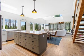 A modern kitchen with a large island, wooden flooring, and large windows offering a view of the outdoors. - Quiet, modern, dog-friendly home with ocean views, private trails & firepit (St. George)