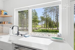 A modern kitchen with a large window, white countertops, a black faucet, and a stone basin. - Quiet, modern, dog-friendly home with ocean views, private trails & firepit (St. George)