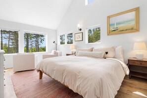 A bedroom with a large bed, a desk, a chair, and a window with a view of trees. - Quiet, modern, dog-friendly home with ocean views, private trails & firepit (St. George)