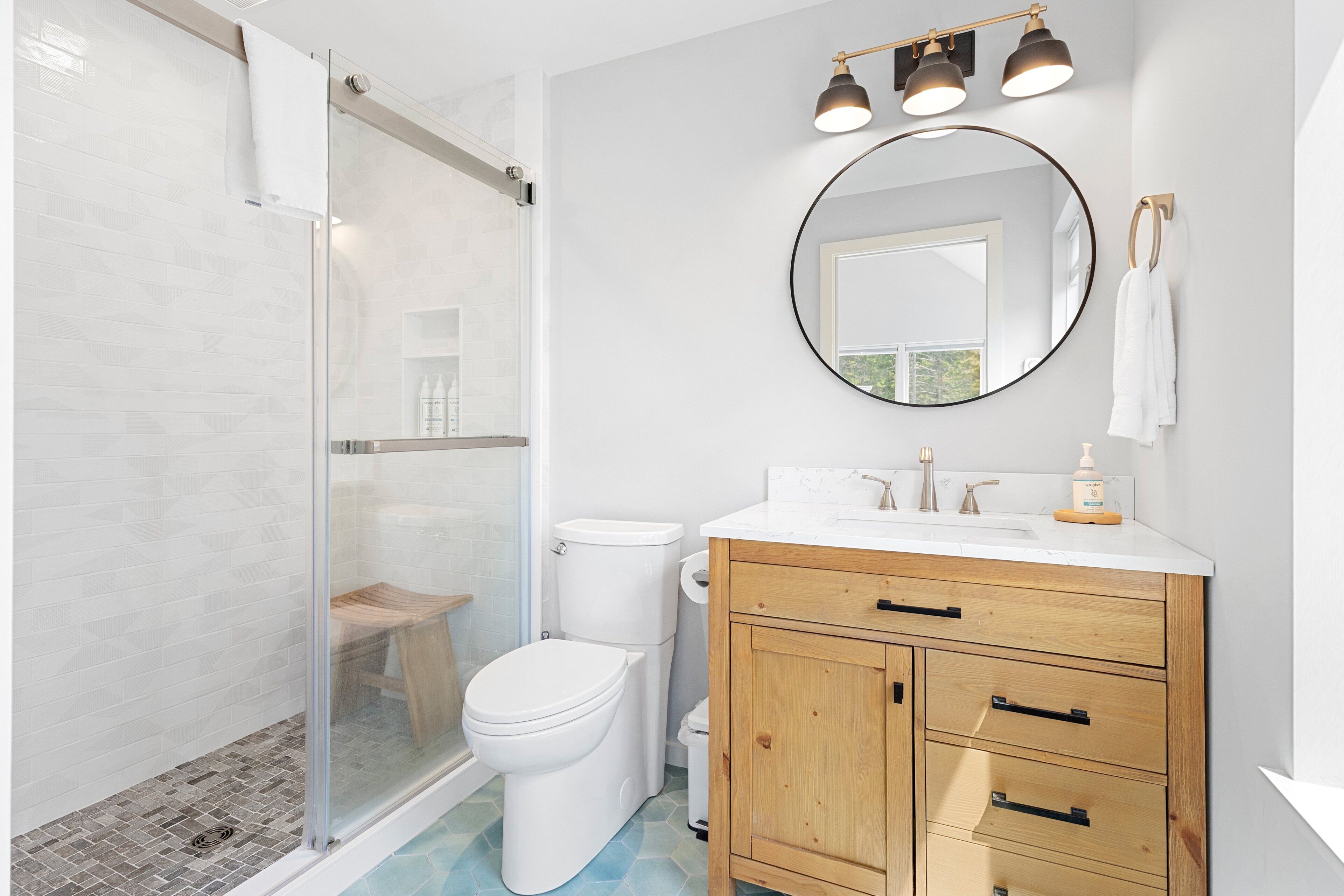 Ein Badezimmer mit Duschkabine aus Glas, Toilette, Waschbecken mit Spiegel und Holzschränken.