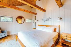 Une chambre à coucher avec un lit en bois, une table de chevet, une commode et un mur orné d’un miroir rond.
