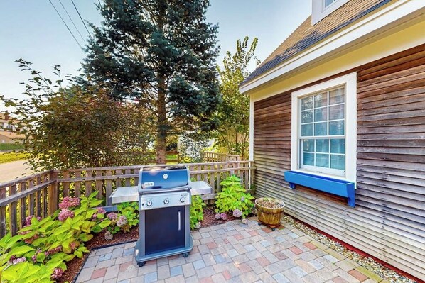 Une terrasse avec un barbecue, une clôture en bois et une maison avec une fenêtre.