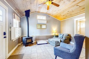 Un salon chaleureux avec une cheminée, un canapé, un fauteuil et un ventilateur de plafond.