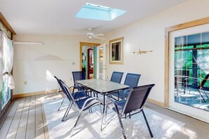 A room with a table and chairs, a ceiling fan, a skylight, and a view through a glass door. - Tree-lined home with screened porch & perfect Midcoast location (Damariscotta)
