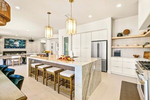 A modern kitchen with a central island, bar stools, stainless steel appliances, and pendant lighting. - Valhalla/Game Room/Waterslide (Indio)