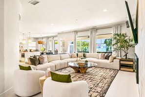 A modern living room with a sectional sofa, a coffee table, and a large window offering a view of the outdoors. - Valhalla/Game Room/Waterslide (Indio)