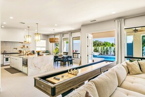 A modern kitchen with a central island, dining area with chairs, and a pool view. - Valhalla/Game Room/Waterslide (Indio)