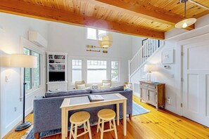Ein modernes Interieur mit Holzbalkendecke, einer Couch, einem Esstisch mit Hockern und einer Treppe.