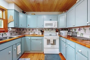 A kitchen with light blue cabinets, a white microwave, a stove, and a toaster.