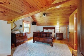 Una camera da letto con soffitto in legno, un letto, una cassettiera, uno specchio e una porta.