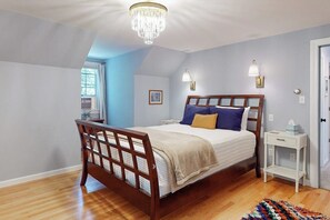 A bedroom with a wooden bed, a chandelier, a bedside table, and a window. - Woodland home with screened porch, 2 living rooms - near historic waterfront (Bath)