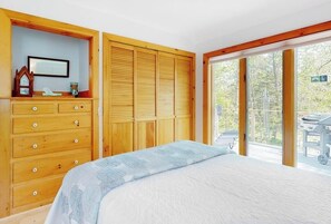 Ein Schlafzimmer mit einem Bett, einer Holzkommode und einer Schiebetür zu einem Außenbereich.