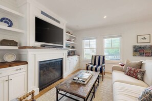 A living room with a fireplace, a television, a striped armchair, and a sofa.
