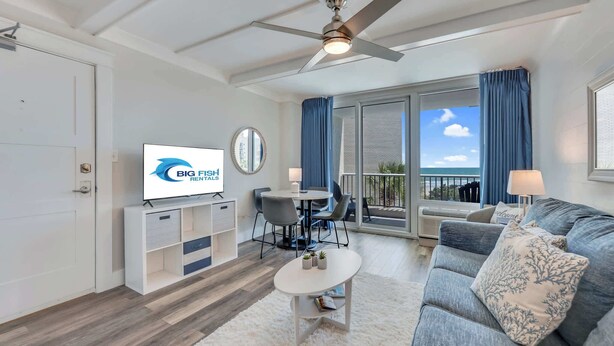 Een moderne woonkamer met een flatscreen televisie, een plafondventilator, een eethoek en een balkon met uitzicht.