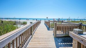 Een houten looppad dat naar een strand leidt, met parasols en mensen.