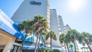 Een hotel met een groot 'Delray'-bord, meerdere verdiepingen en palmbomen ervoor.