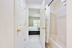 Ein schmaler Flur führt zu einem Schlafzimmer mit Bett und Badewanne.