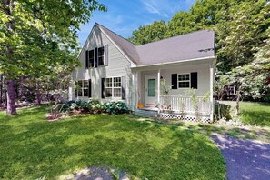 A two-story house with a porch, surrounded by a well-maintained lawn and trees. - Peaceful home with forest views & great yard - minutes to town (Wiscasset)