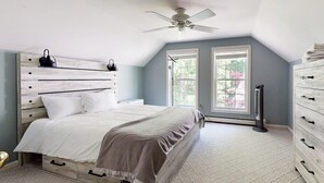 Une chambre à coucher avec un lit, un ventilateur de plafond, une commode et deux fenêtres.