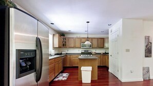Une cuisine moderne avec des meubles en bois, un réfrigérateur en acier inoxydable, un îlot central et un luminaire suspendu.